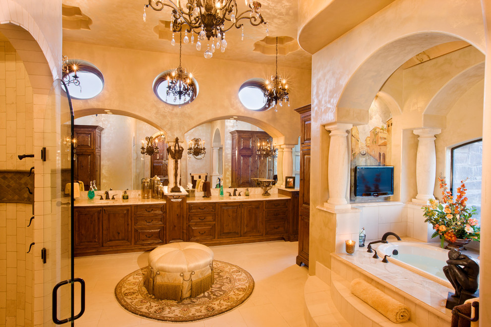Idée de décoration pour une très grande salle de bain principale méditerranéenne en bois foncé avec une baignoire posée, un carrelage beige, un carrelage de pierre, un mur beige, un sol en travertin, un lavabo encastré, un plan de toilette en granite et un placard avec porte à panneau surélevé.