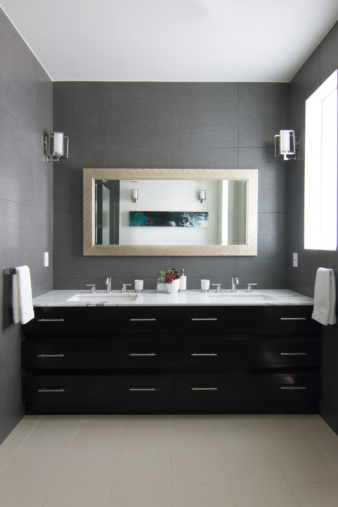 На фото: ванная комната в современном стиле с врезной раковиной, темными деревянными фасадами, мраморной столешницей, бежевой плиткой, каменной плиткой и плоскими фасадами