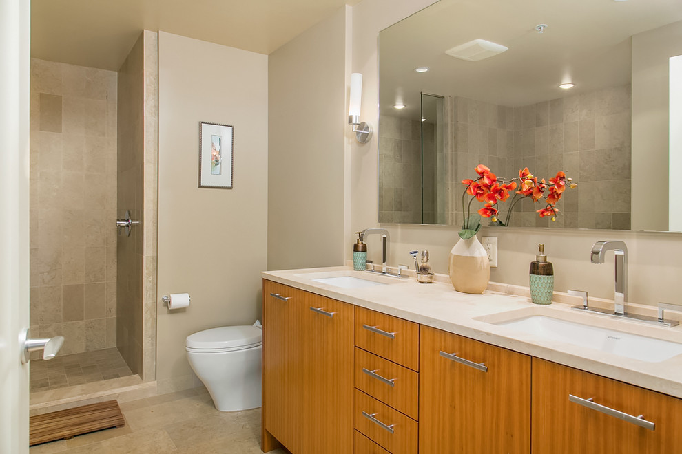 Example of a large trendy master beige tile ceramic tile bathroom design in Seattle with flat-panel cabinets, medium tone wood cabinets, a one-piece toilet, beige walls, an undermount sink and solid surface countertops