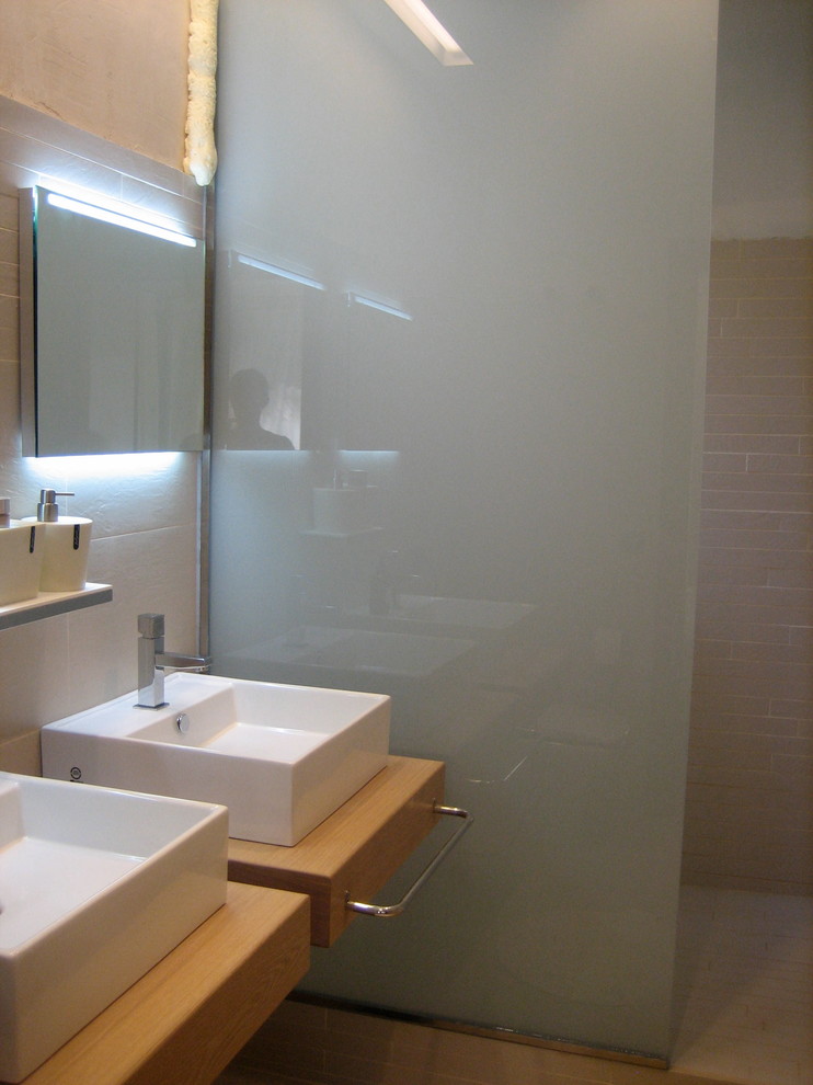 Inredning av ett modernt mellanstort badrum med dusch, med ett väggmonterat handfat, släta luckor, skåp i mellenmörkt trä, träbänkskiva, ett platsbyggt badkar, en dubbeldusch, en toalettstol med hel cisternkåpa, beige kakel, porslinskakel, beige väggar och klinkergolv i porslin