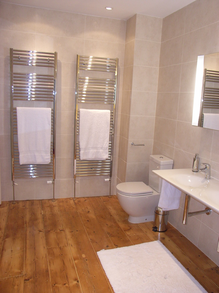 Medium sized contemporary ensuite bathroom in Other with a wall-mounted sink, a two-piece toilet, beige tiles, ceramic tiles and light hardwood flooring.