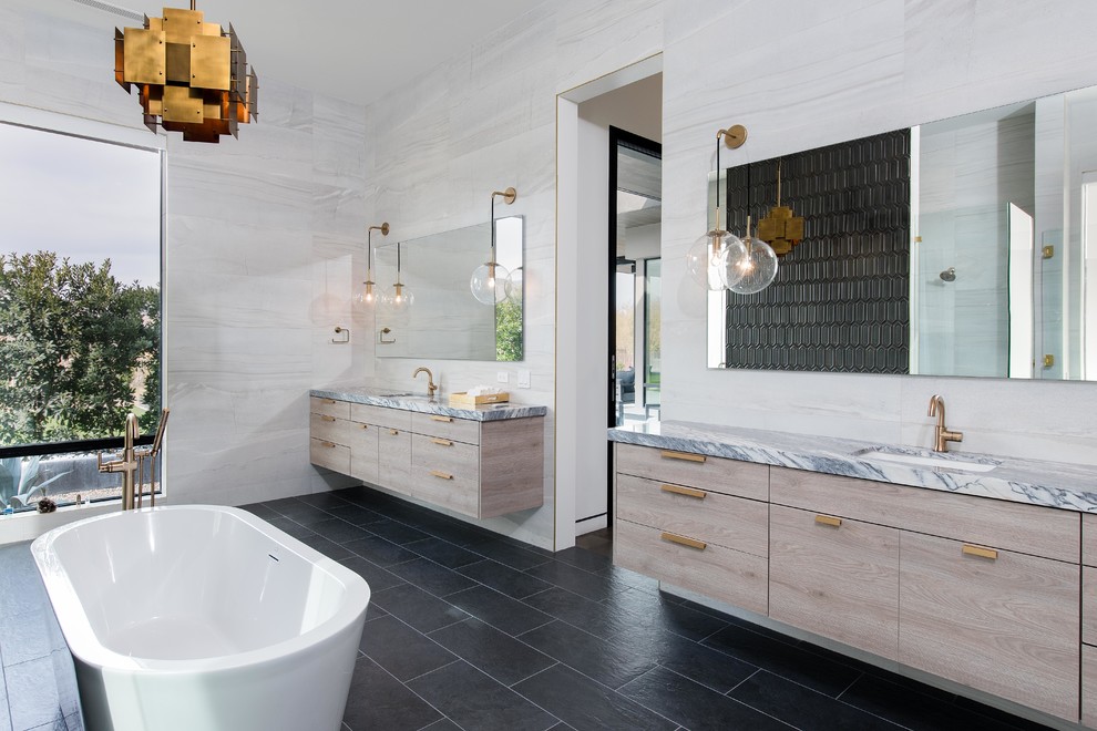 Idées déco pour une salle de bain principale contemporaine en bois clair avec un placard à porte plane, un lavabo encastré, un plan de toilette en marbre, un plan de toilette multicolore, une baignoire indépendante, un carrelage blanc et un sol noir.