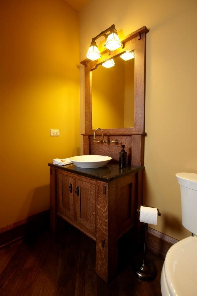 Foto de cuarto de baño de estilo americano pequeño con sanitario de una pieza, paredes amarillas, suelo de madera oscura, armarios estilo shaker, puertas de armario de madera en tonos medios y lavabo sobreencimera