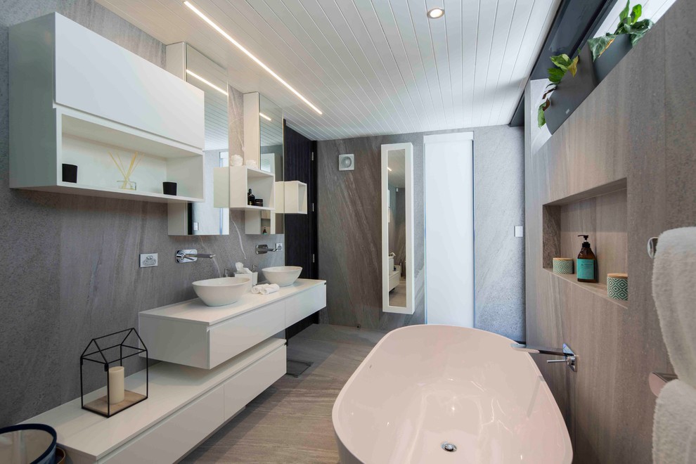 Großes Modernes Badezimmer En Suite mit weißen Schränken, freistehender Badewanne, grauen Fliesen und braunem Holzboden in Sunshine Coast