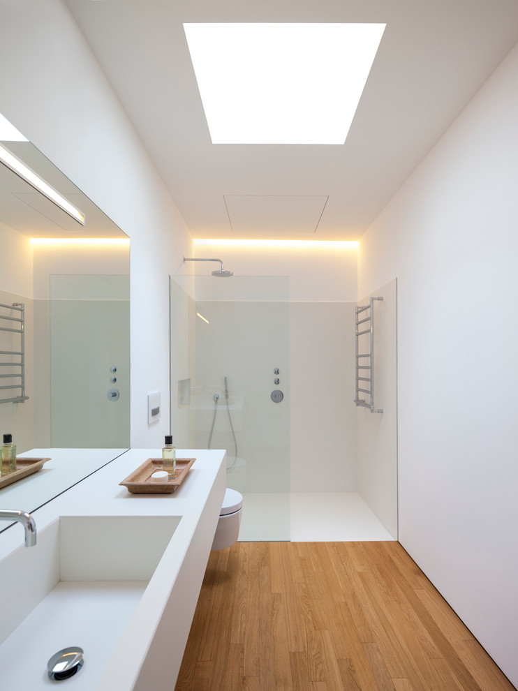 Diseño de cuarto de baño principal actual pequeño con lavabo integrado, ducha a ras de suelo, sanitario de pared, paredes blancas y suelo de madera en tonos medios