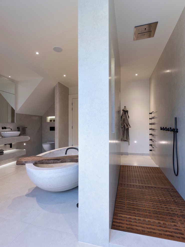 Inredning av ett modernt stort vit vitt en-suite badrum, med släta luckor, vita skåp, ett fristående badkar, en öppen dusch, en vägghängd toalettstol, porslinskakel, vita väggar, klinkergolv i porslin, ett avlångt handfat, kaklad bänkskiva, vitt golv och med dusch som är öppen