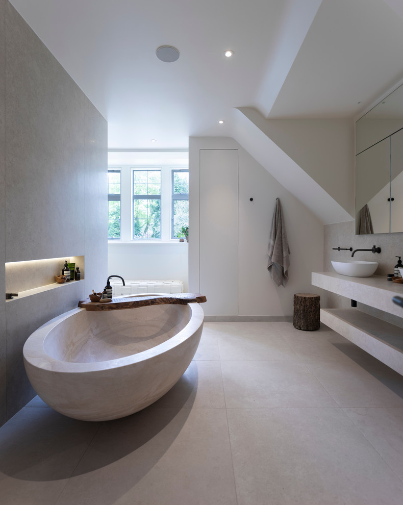Modern inredning av ett stort vit vitt en-suite badrum, med släta luckor, vita skåp, ett fristående badkar, en vägghängd toalettstol, porslinskakel, vita väggar, klinkergolv i porslin, kaklad bänkskiva, vitt golv och ett fristående handfat