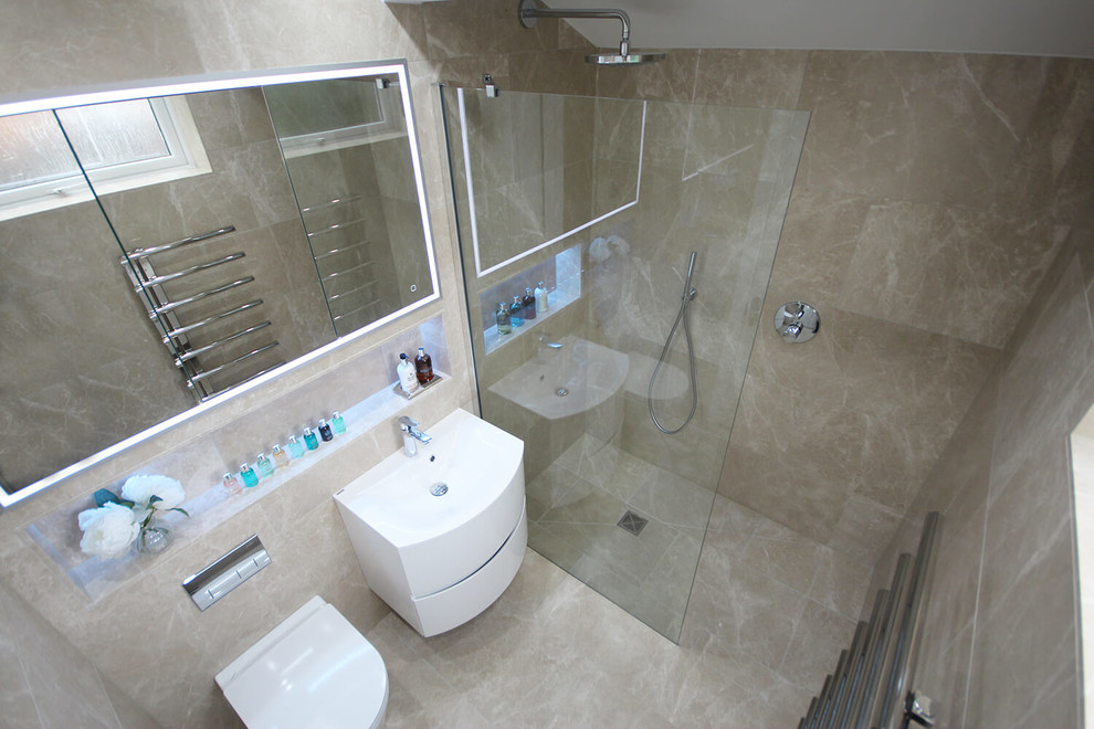 This is an example of a small modern ensuite bathroom in Surrey with a walk-in shower, a wall mounted toilet, beige tiles, marble tiles, beige walls, marble flooring, a built-in sink and beige floors.