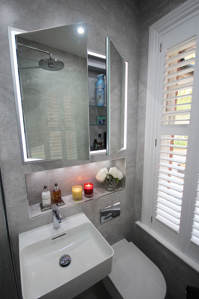 Modern inredning av ett litet en-suite badrum, med en öppen dusch, en vägghängd toalettstol, grå kakel, porslinskakel, grå väggar, klinkergolv i porslin, ett väggmonterat handfat, grått golv och med dusch som är öppen