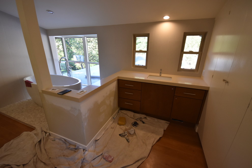 This is an example of a large modern ensuite bathroom in Los Angeles with flat-panel cabinets, medium wood cabinets, a freestanding bath, a corner shower, a one-piece toilet, beige tiles, porcelain tiles, beige walls, pebble tile flooring, a submerged sink, copper worktops and beige floors.