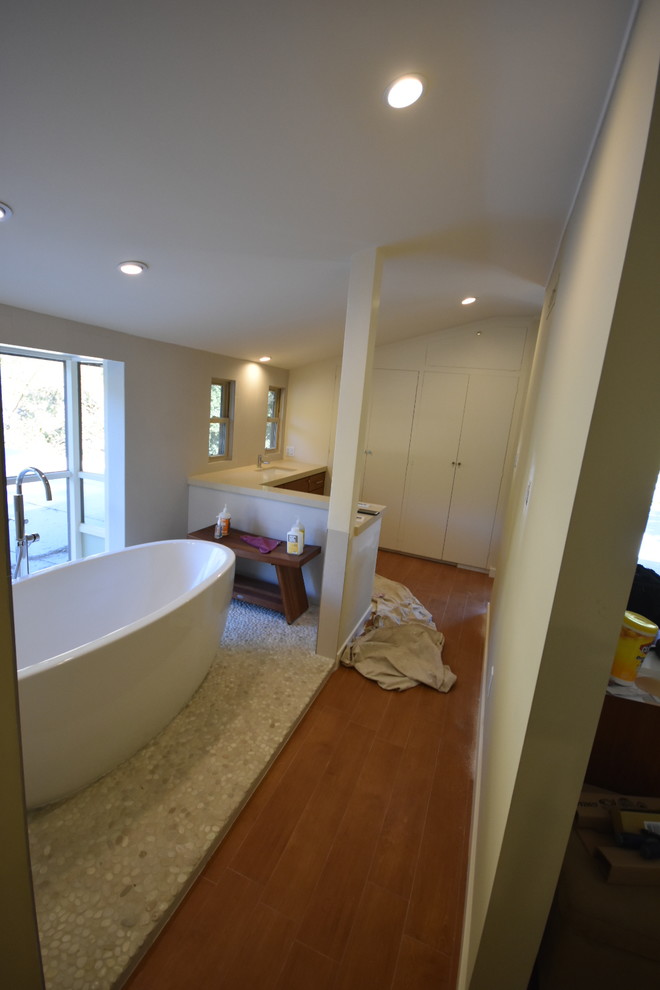 This is an example of a large modern ensuite bathroom in Los Angeles with flat-panel cabinets, medium wood cabinets, a freestanding bath, a corner shower, a one-piece toilet, beige tiles, porcelain tiles, beige walls, pebble tile flooring, a submerged sink, copper worktops and beige floors.