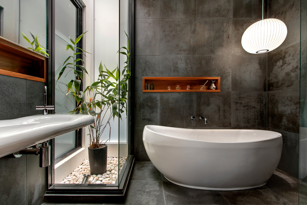 Modern inredning av ett litet en-suite badrum, med ett fristående badkar, en öppen dusch, en toalettstol med hel cisternkåpa, svart kakel, stenkakel, svarta väggar och ett väggmonterat handfat
