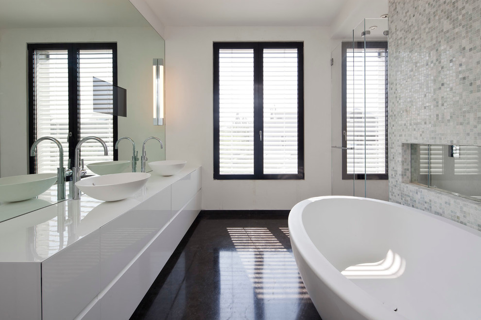 Inspiration för stora moderna en-suite badrum, med ett konsol handfat, möbel-liknande, vita skåp, bänkskiva i akrylsten, ett fristående badkar, en dubbeldusch, en vägghängd toalettstol, flerfärgad kakel, mosaik och vita väggar