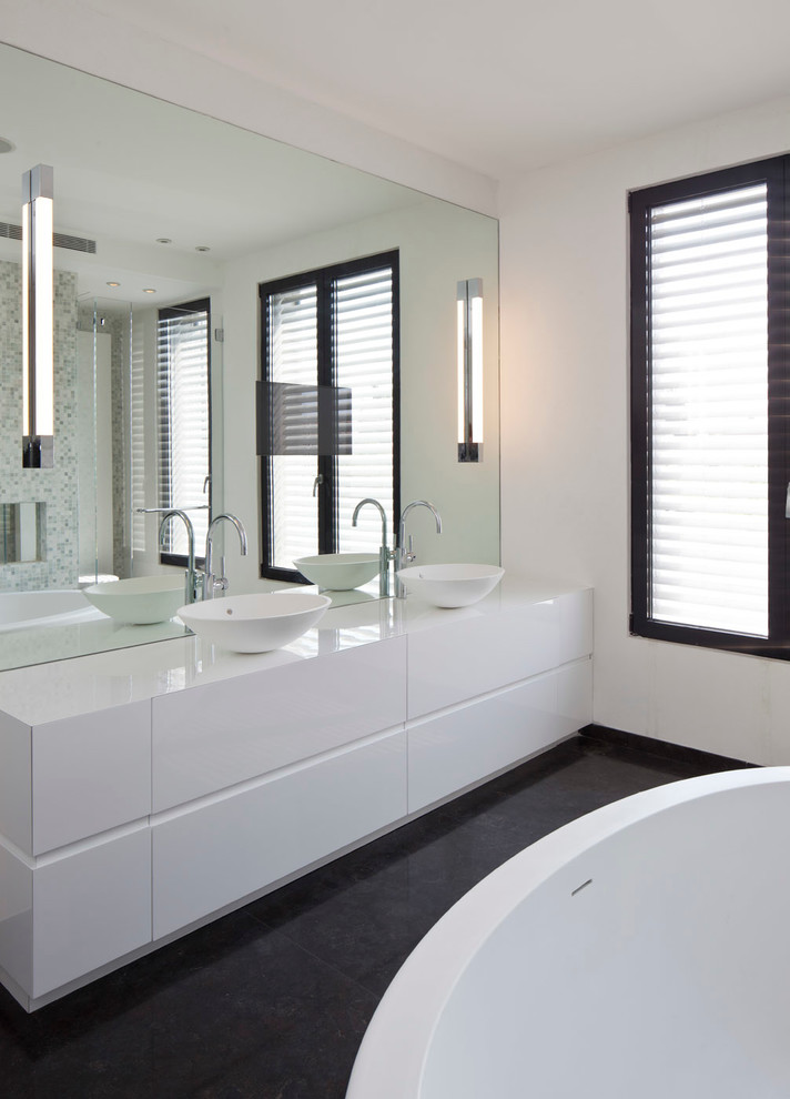 Inspiration for a large modern ensuite bathroom in Other with freestanding cabinets, white cabinets, a freestanding bath, a wall mounted toilet, multi-coloured tiles, mosaic tiles and white walls.
