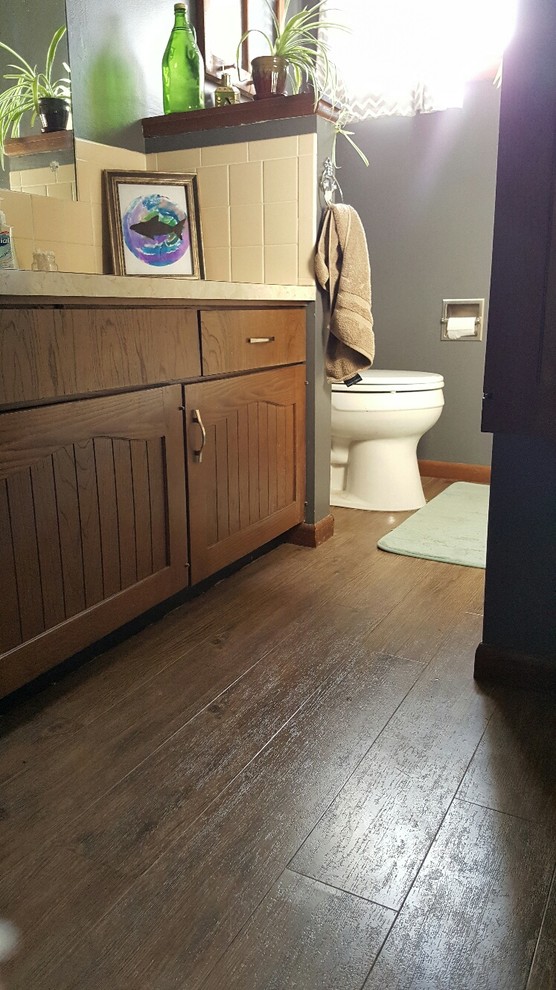 Lantlig inredning av ett litet badrum med dusch, med luckor med infälld panel, bruna skåp, ett platsbyggt badkar, en toalettstol med separat cisternkåpa, gul kakel, keramikplattor, grå väggar, vinylgolv, ett nedsänkt handfat och laminatbänkskiva