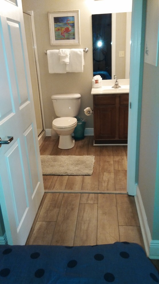 Maritim inredning av ett mellanstort vit vitt badrum med dusch, med skåp i mörkt trä, en dusch i en alkov, en toalettstol med separat cisternkåpa, beige väggar, ljust trägolv, ett integrerad handfat, bänkskiva i akrylsten, brunt golv och dusch med skjutdörr