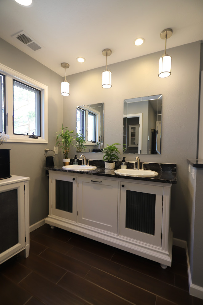 This is an example of a medium sized modern ensuite bathroom in Denver with glass-front cabinets, white cabinets, a built-in bath, an alcove shower, a bidet, white tiles, porcelain tiles, grey walls, porcelain flooring, a submerged sink, soapstone worktops, brown floors, a hinged door and black worktops.