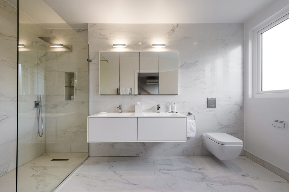 Exemple d'une salle de bain principale moderne avec un placard à porte plane, des portes de placard blanches, une douche ouverte, WC suspendus, un carrelage gris, un carrelage blanc, un mur multicolore, un lavabo intégré et aucune cabine.