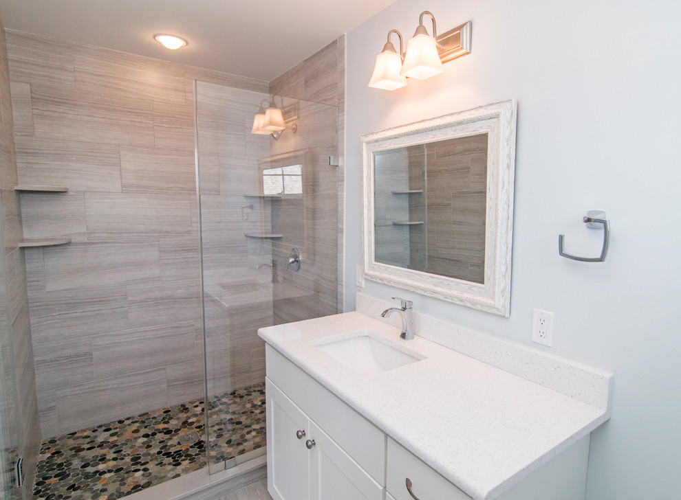 Doorless shower - mid-sized coastal master gray tile and pebble tile ceramic tile doorless shower idea in New York with shaker cabinets, white cabinets, blue walls, an undermount sink, a one-piece toilet and quartz countertops
