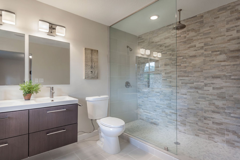 Photo of a large midcentury ensuite bathroom in Tampa with a trough sink, flat-panel cabinets, dark wood cabinets, solid surface worktops, a walk-in shower, a one-piece toilet, multi-coloured tiles, stone tiles, beige walls, porcelain flooring and a freestanding bath.