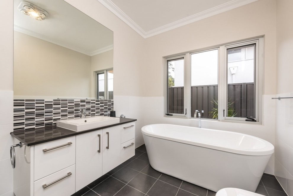 Example of a trendy 3/4 white tile gray floor freestanding bathtub design in Adelaide with flat-panel cabinets, white cabinets, beige walls, a drop-in sink and gray countertops