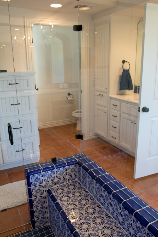 Inspiration for a large mediterranean ensuite bathroom in Austin with recessed-panel cabinets, white cabinets, an alcove shower, blue tiles, ceramic tiles, white walls, terracotta flooring, a submerged sink, marble worktops, brown floors, a hinged door and white worktops.