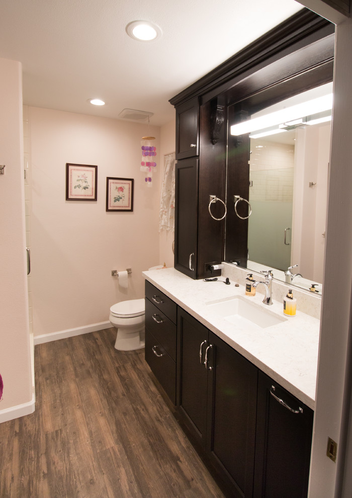 Cette image montre une salle de bain principale traditionnelle en bois foncé de taille moyenne avec un placard à porte plane, WC séparés, un carrelage blanc, un carrelage métro, un mur rose, un lavabo encastré, un plan de toilette en quartz modifié et un sol marron.