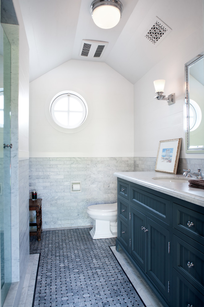 Modelo de cuarto de baño tradicional grande con lavabo bajoencimera, armarios con paneles empotrados, puertas de armario grises, encimera de mármol, ducha empotrada, baldosas y/o azulejos grises, paredes blancas y suelo de mármol