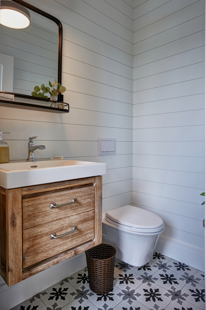 Maritim inredning av ett litet vit vitt badrum, med en vägghängd toalettstol, vita väggar, cementgolv, ett konsol handfat och flerfärgat golv