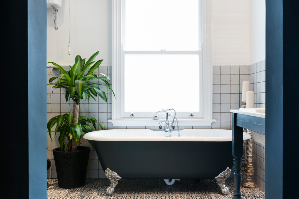 Modelo de cuarto de baño actual con bañera con patas, paredes blancas, suelo con mosaicos de baldosas y lavabo tipo consola