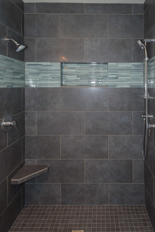 Modern inredning av ett badrum, med en dusch i en alkov, en toalettstol med separat cisternkåpa, grå kakel, stenkakel och dusch med gångjärnsdörr