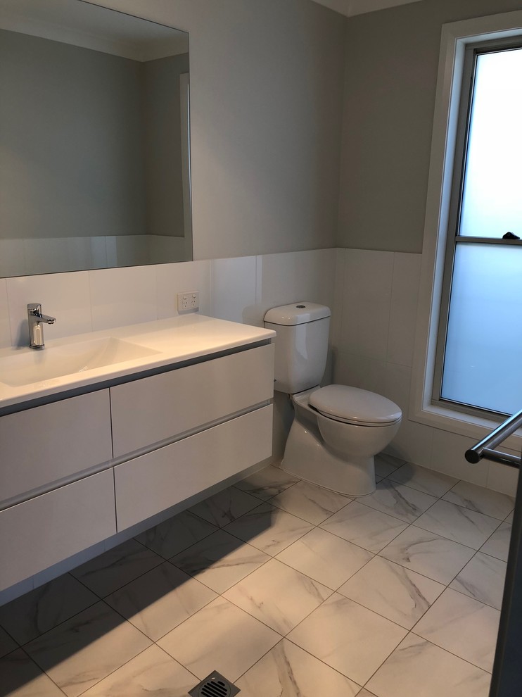 Exempel på ett mellanstort modernt vit vitt badrum med dusch, med en toalettstol med hel cisternkåpa, vit kakel, porslinskakel, grå väggar, klinkergolv i porslin, grått golv, dusch med gångjärnsdörr, luckor med infälld panel, grå skåp och bänkskiva i akrylsten