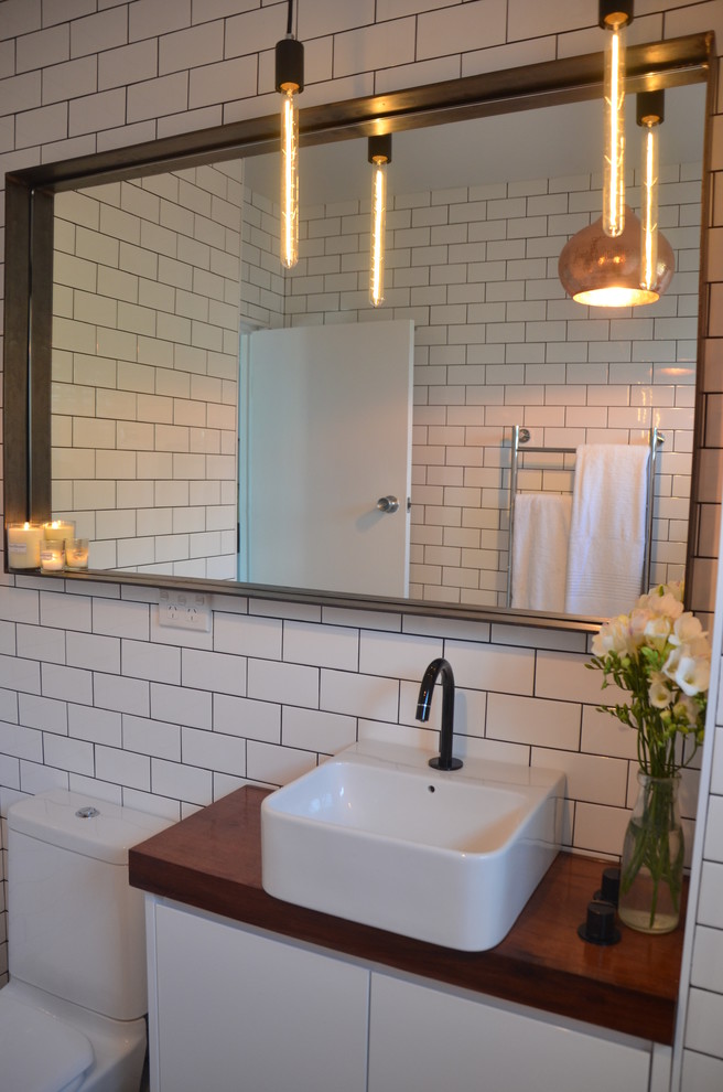 Стильный дизайн: ванная комната в современном стиле с настольной раковиной, ванной в нише, душем над ванной, раздельным унитазом, плоскими фасадами, белыми фасадами, столешницей из дерева, белой плиткой и керамической плиткой - последний тренд
