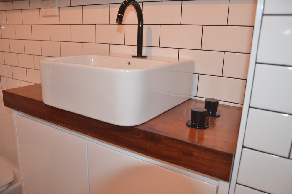 Exempel på ett modernt badrum, med ett fristående handfat, ett badkar i en alkov, en dusch/badkar-kombination, en toalettstol med hel cisternkåpa, släta luckor, vita skåp, träbänkskiva, vit kakel och keramikplattor