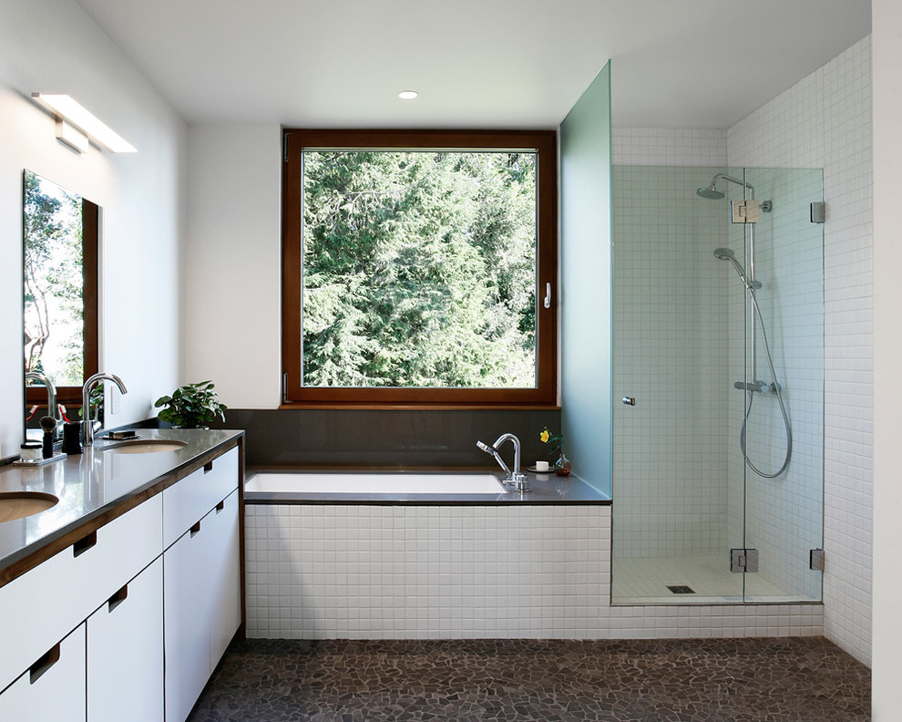 Modern inredning av ett badrum, med ett undermonterad handfat, släta luckor, vita skåp, ett undermonterat badkar, vit kakel och vita väggar