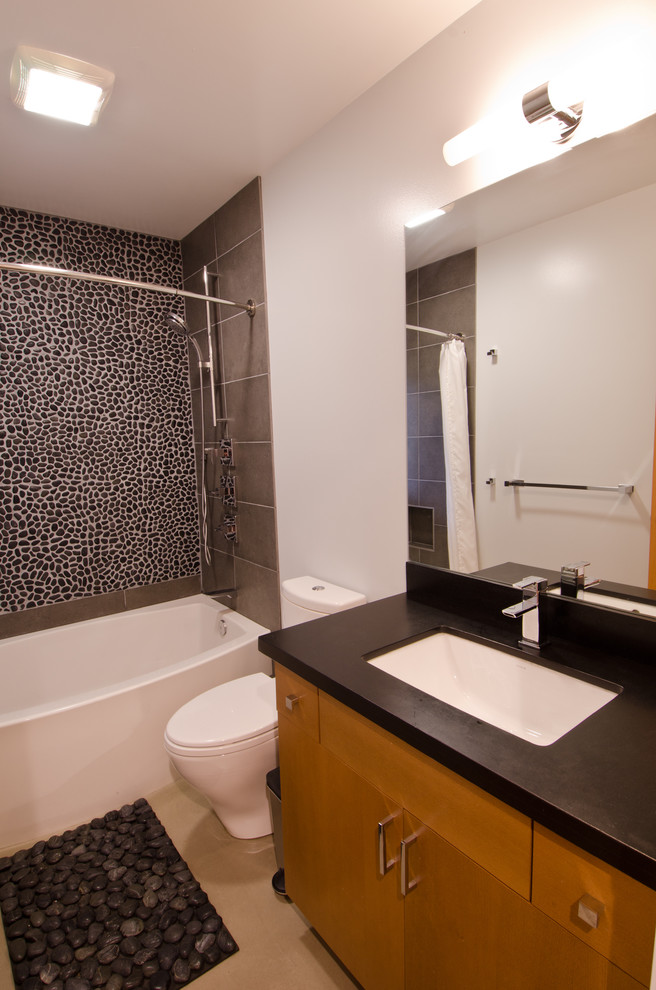 Idéer för att renovera ett mellanstort funkis badrum med dusch, med släta luckor, skåp i mellenmörkt trä, ett badkar i en alkov, en dusch/badkar-kombination, en toalettstol med separat cisternkåpa, svart kakel, kakel i småsten, vita väggar och ett undermonterad handfat