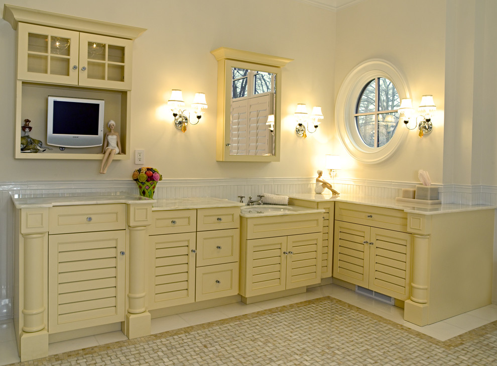 На фото: большая главная ванная комната в классическом стиле с фасадами с филенкой типа жалюзи, желтыми фасадами, отдельно стоящей ванной, угловым душем, белой плиткой, мраморной плиткой, бежевыми стенами, мраморным полом, врезной раковиной, столешницей из оникса, разноцветным полом и душем с распашными дверями с