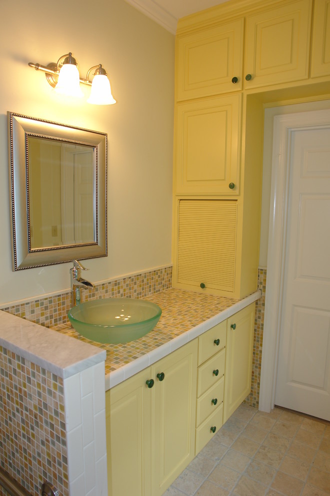 Maritim inredning av ett litet en-suite badrum, med gula skåp, en dusch i en alkov, en toalettstol med separat cisternkåpa, gul kakel, glaskakel, vita väggar, klinkergolv i keramik, ett fristående handfat och bänkskiva i glas