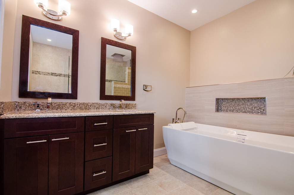 This is an example of a contemporary ensuite bathroom in DC Metro with recessed-panel cabinets, dark wood cabinets, engineered stone worktops, beige tiles, a freestanding bath, a built-in shower, a submerged sink and beige walls.