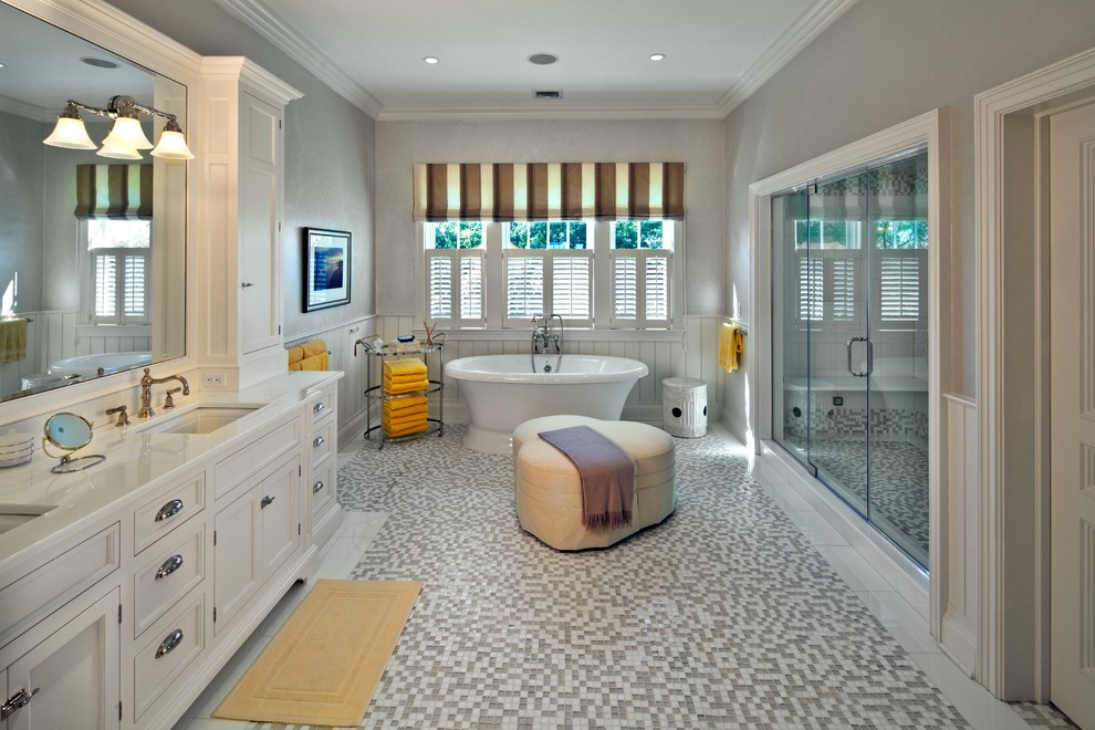 Diseño de cuarto de baño tradicional con lavabo bajoencimera, puertas de armario blancas, bañera exenta, ducha empotrada, paredes grises, suelo con mosaicos de baldosas y armarios con paneles empotrados