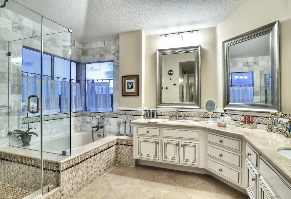 На фото: большая главная ванная комната в классическом стиле с фасадами с выступающей филенкой, искусственно-состаренными фасадами, гидромассажной ванной, душем в нише, унитазом-моноблоком, белой плиткой, мраморной плиткой, белыми стенами, полом из известняка, врезной раковиной, столешницей из известняка, бежевым полом, душем с распашными дверями, бежевой столешницей, сиденьем для душа, тумбой под две раковины, встроенной тумбой и сводчатым потолком