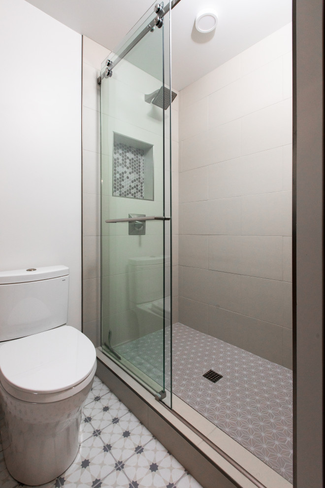 Идея дизайна: маленькая главная ванная комната в стиле неоклассика (современная классика) с плоскими фасадами, синими фасадами, душем в нише, раздельным унитазом, бежевой плиткой, керамогранитной плиткой, белыми стенами, полом из керамогранита, врезной раковиной, столешницей из искусственного кварца, разноцветным полом, душем с раздвижными дверями, черной столешницей, тумбой под одну раковину и встроенной тумбой для на участке и в саду