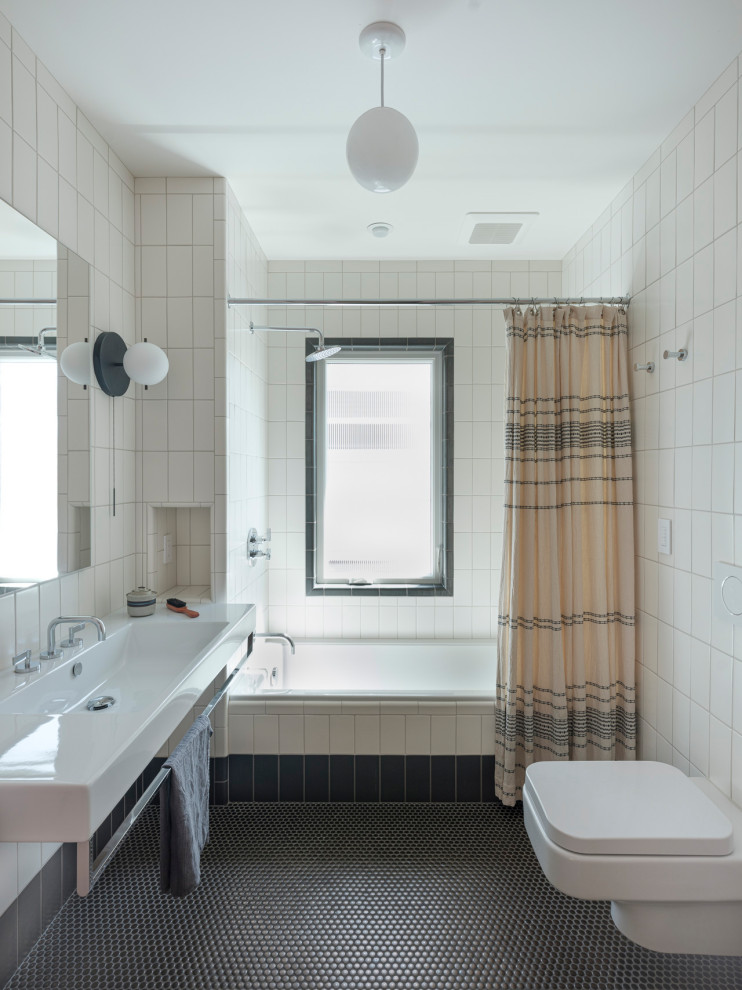 Modern inredning av ett badrum, med ett badkar i en alkov, en dusch/badkar-kombination, en vägghängd toalettstol, vit kakel, mosaikgolv, ett väggmonterat handfat, grått golv och dusch med duschdraperi