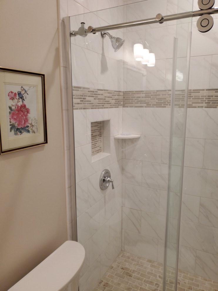 Klassisk inredning av ett litet badrum, med vita skåp, en dusch i en alkov, en toalettstol med separat cisternkåpa, beige väggar, klinkergolv i porslin, bänkskiva i kvartsit och dusch med skjutdörr