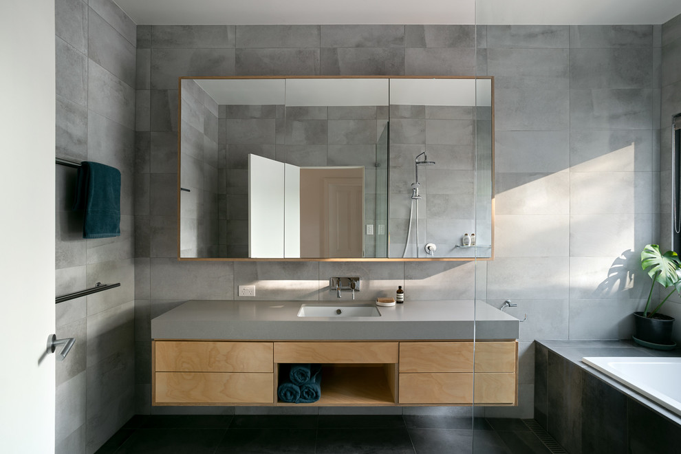 Идея дизайна: ванная комната среднего размера в современном стиле с плоскими фасадами, светлыми деревянными фасадами, накладной ванной, открытым душем, унитазом-моноблоком, серой плиткой, керамической плиткой, серыми стенами, полом из керамической плитки, врезной раковиной, серым полом, открытым душем и серой столешницей