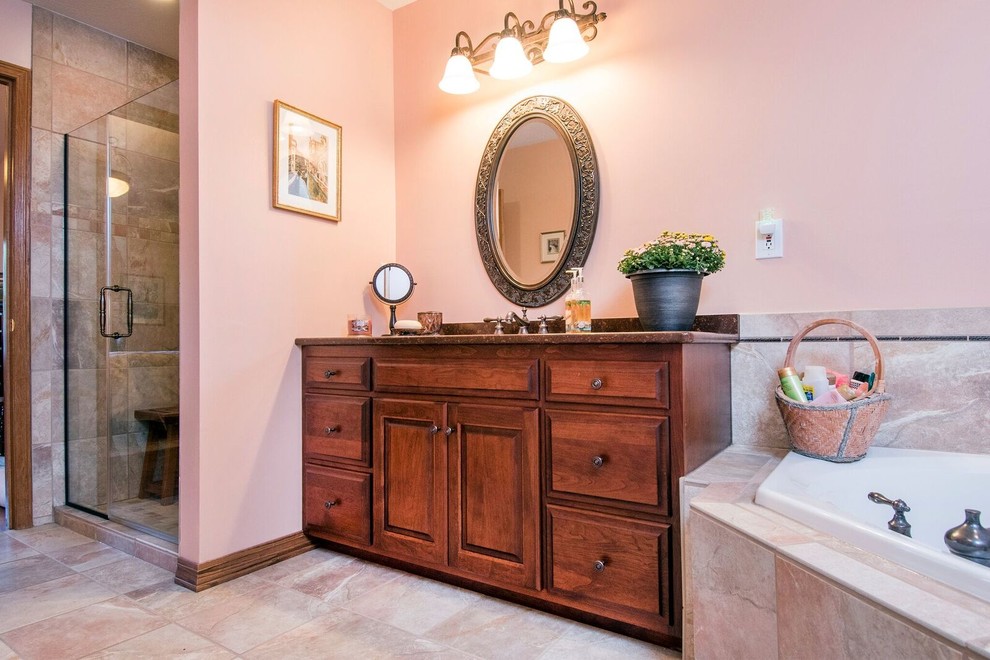 This is an example of a medium sized classic ensuite bathroom in Cincinnati with raised-panel cabinets, dark wood cabinets, a corner bath, a corner shower, a two-piece toilet, beige tiles, porcelain tiles, pink walls, porcelain flooring, a submerged sink, granite worktops, beige floors, a hinged door and brown worktops.