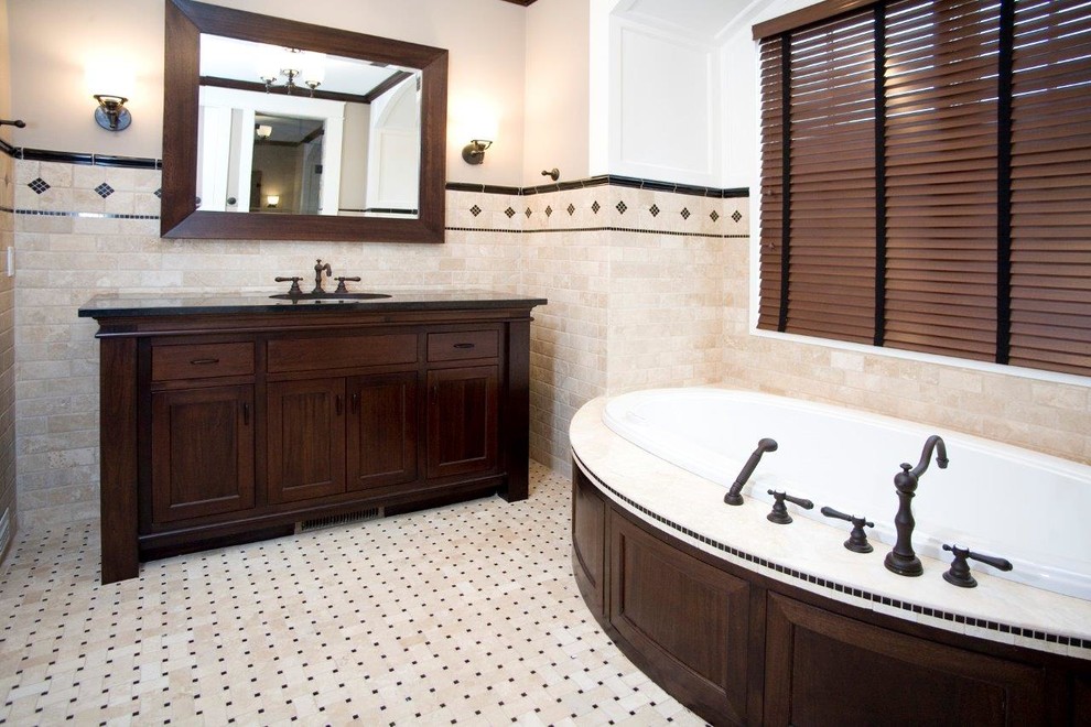 Klassisk inredning av ett mellanstort en-suite badrum, med luckor med profilerade fronter, skåp i mörkt trä, ett platsbyggt badkar, beige kakel, ett undermonterad handfat, granitbänkskiva, beige väggar, klinkergolv i keramik och beiget golv