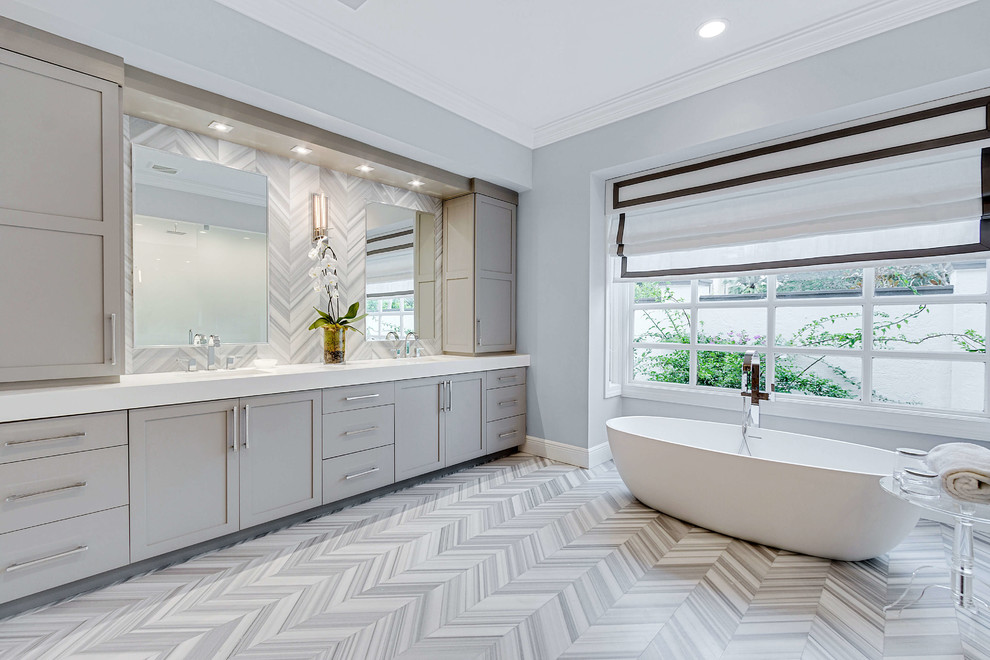 This is an example of a medium sized classic ensuite bathroom in Miami with shaker cabinets, grey cabinets, a freestanding bath, grey walls, grey floors, white worktops, an alcove shower, porcelain flooring, a submerged sink, solid surface worktops and a hinged door.