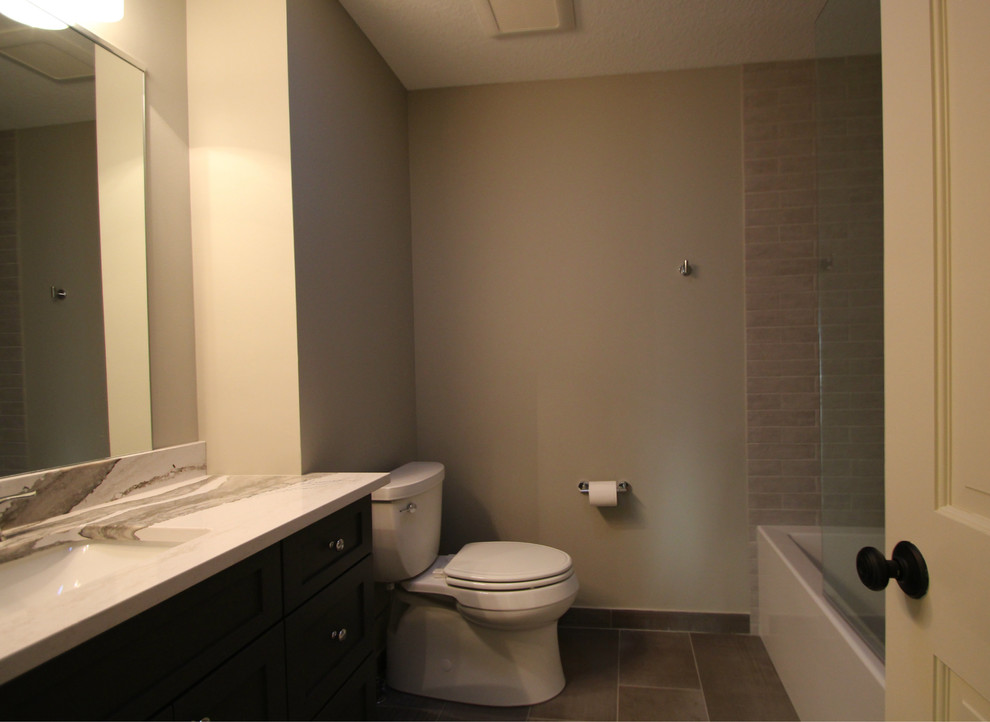 Inredning av ett modernt mellanstort vit vitt badrum med dusch, med skåp i shakerstil, grå skåp, ett badkar i en alkov, en dusch/badkar-kombination, en toalettstol med separat cisternkåpa, grå kakel, grå väggar, klinkergolv i keramik, ett undermonterad handfat, bänkskiva i kvarts, grått golv och dusch med gångjärnsdörr