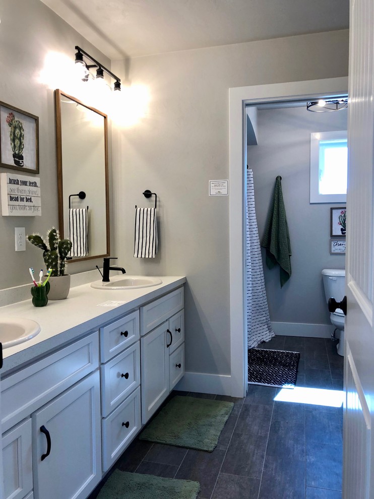 Bathroom - mid-sized cottage kids' vinyl floor and black floor bathroom idea in Other with shaker cabinets, white cabinets, a one-piece toilet, gray walls, a drop-in sink, laminate countertops and white countertops